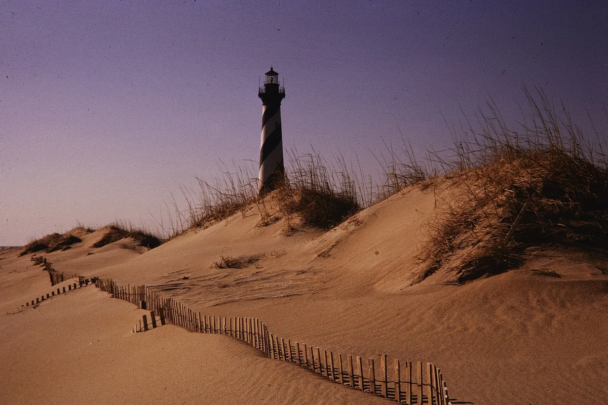 Cape Hatteras Lighthouse behind sand dunes and a sand fence on Hatteras Island