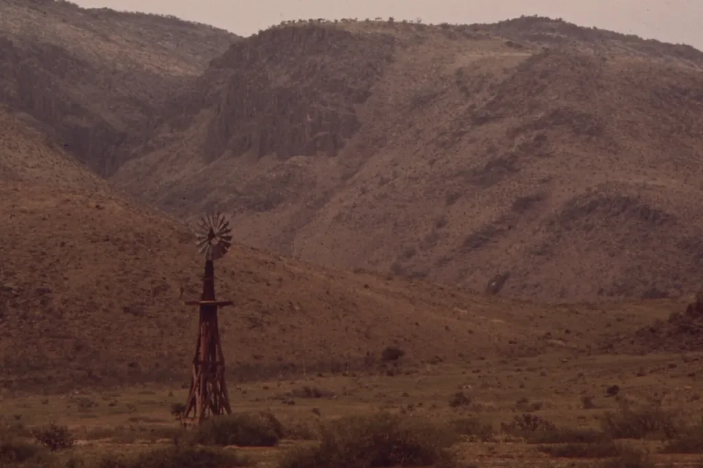 A wooden windmill stands below dry, rugged slopes in the Davis Mountains of West Texas